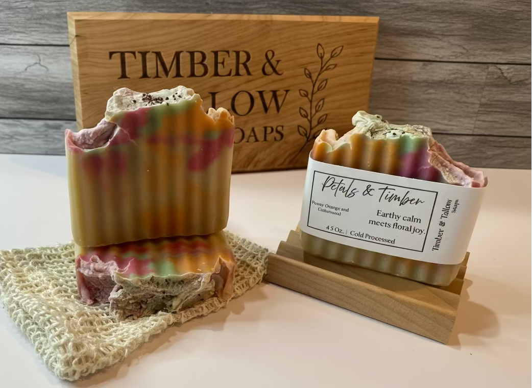 Two soap bars with a wooden stand and 'Timber & Tallow Soaps' branding in the background.