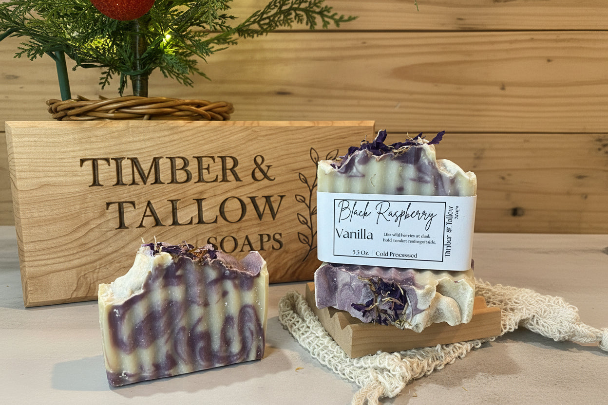 Two bars of soap with a 'Black Raspberry Vanilla' label on a wooden stand, with 'Timber & Tallow Soaps' branding in the background.