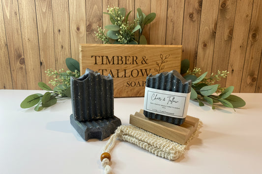 Bar of soap with a wooden stand and candle on a white surface with 'Timber & Tallow' branding.