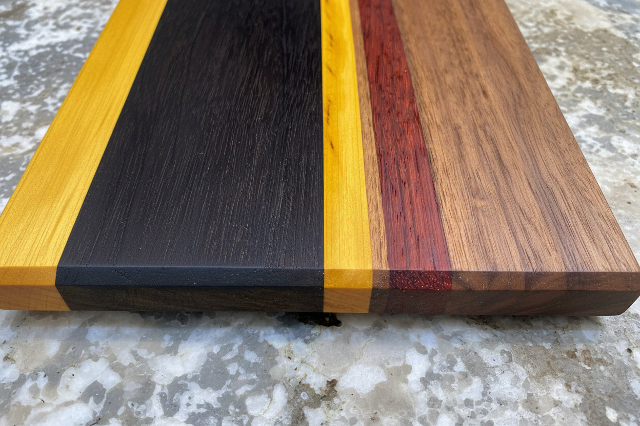 Wooden cutting board with black, yellow, and red stripes on a textured surface